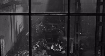Movie still from “Schindler's List” (1993), directed by Steven Spielberg – A black and white photo of people sitting in a building; Wide shot, High angle
