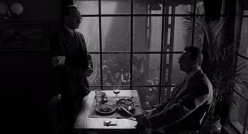 Movie still from “Schindler's List” (1993), directed by Steven Spielberg – Two men are sitting at a table in front of a window; Medium shot, Over the shoulder angle