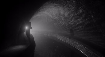 Movie still from “Schindler's List” (1993), directed by Steven Spielberg – A man is standing in a tunnel with a flashlight; Extreme Wide shot, High angle