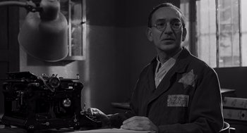 Movie still from “Schindler's List” (1993), directed by Steven Spielberg – An older man sitting in front of a sewing machine; Medium shot, Low angle