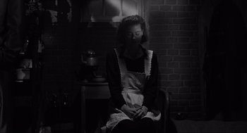 Movie still from “Schindler's List” (1993), directed by Steven Spielberg – A woman sitting in a chair wearing an apron; Medium shot, Low angle
