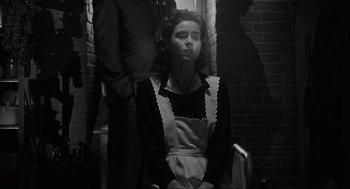 Movie still from “Schindler's List” (1993), directed by Steven Spielberg – A woman in an apron sitting in front of a man; Medium shot, Low angle