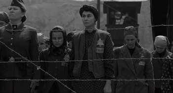 Movie still from “Schindler's List” (1993), directed by Steven Spielberg – A group of people standing next to a barbed wire fence; Medium shot, Low angle