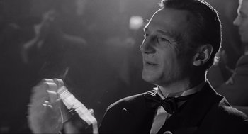 Movie still from “Schindler's List” (1993), directed by Steven Spielberg – A black and white photo of a man smoking a cigarette and holding a cell phone; Close Up shot, Over the shoulder angle