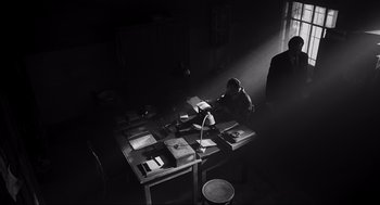 Movie still from “Schindler's List” (1993), directed by Steven Spielberg – A man sitting at a table with papers on top of it; Wide shot, High angle
