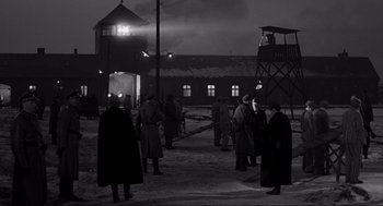 Movie still from “Schindler's List” (1993), directed by Steven Spielberg – A black and white photo of a group of people standing outside; Extreme Wide shot, Over the shoulder angle