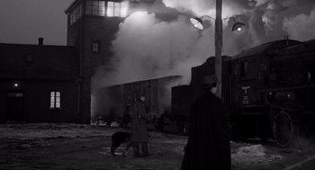 Movie still from “Schindler's List” (1993), directed by Steven Spielberg – Two men and a dog stand in front of a steam train; Extreme Wide shot, Over the shoulder angle