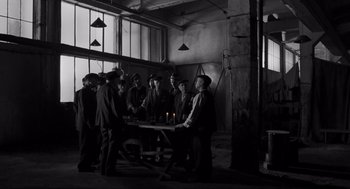 Movie still from “Schindler's List” (1993), directed by Steven Spielberg – A group of men standing around a table with a lit candle; Wide shot, High angle