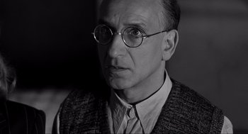 Movie still from “Schindler's List” (1993), directed by Steven Spielberg – An older man wearing glasses and a sweater vest; Close Up shot, Low angle