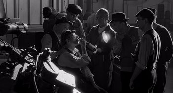 Movie still from “Schindler's List” (1993), directed by Steven Spielberg – A group of men standing next to each other on a bench; Medium shot, High angle