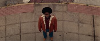 Movie still from “BlacKkKlansman” (2018), directed by Spike Lee – A man standing on the sidewalk wearing a red jacket; Medium shot, High angle