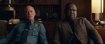 Movie still from “BlacKkKlansman” (2018), directed by Spike Lee – Two men sitting next to each other in front of a wooden table; Close Up shot, Low angle