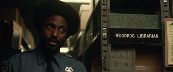 Movie still from “BlacKkKlansman” (2018), directed by Spike Lee – A man in a police uniform standing in front of records; Close Up shot, Over the shoulder angle