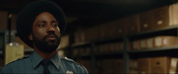 Movie still from “BlacKkKlansman” (2018), directed by Spike Lee – A man in a police uniform standing next to a bookshelf; Close Up shot, Over the shoulder angle