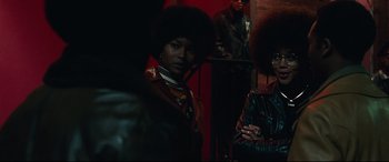 Movie still from “BlacKkKlansman” (2018), directed by Spike Lee – A group of people standing next to each other in a room; Medium shot, Over the shoulder angle
