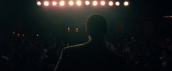 Movie still from “BlacKkKlansman” (2018), directed by Spike Lee – A man is standing in front of a crowd of onlookers; Medium shot, Over the shoulder angle