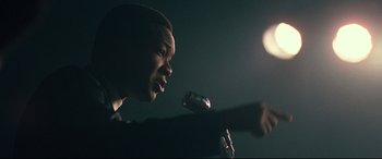 Movie still from “BlacKkKlansman” (2018), directed by Spike Lee – A man is speaking into a microphone in the dark; Close Up shot, Low angle