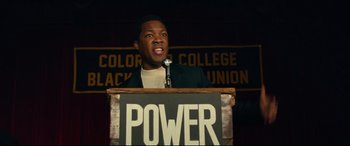 Movie still from “BlacKkKlansman” (2018), directed by Spike Lee – A man standing at a podium with a microphone; Medium shot, Low angle