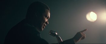 Movie still from “BlacKkKlansman” (2018), directed by Spike Lee – A man is speaking into a microphone in the dark; Close Up shot, Low angle