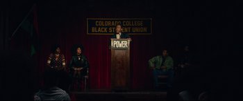 Movie still from “BlacKkKlansman” (2018), directed by Spike Lee – A man standing at a podium on a stage; Wide shot, High angle