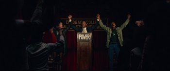 Movie still from “BlacKkKlansman” (2018), directed by Spike Lee – Three people holding their hands in the air at a podium; Wide shot, Low angle