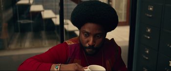 Movie still from “BlacKkKlansman” (2018), directed by Spike Lee – A man with a beard is holding a cup of coffee; Close Up shot, Over the shoulder angle