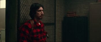 Movie still from “BlacKkKlansman” (2018), directed by Spike Lee – A man wearing a red and black shirt standing next to a wall; Medium shot, Over the shoulder angle