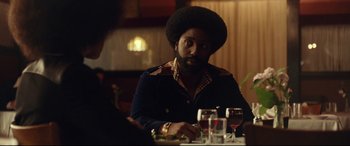 Movie still from “BlacKkKlansman” (2018), directed by Spike Lee – A man sitting at a table with a glass in front of him; Medium shot, Over the shoulder angle