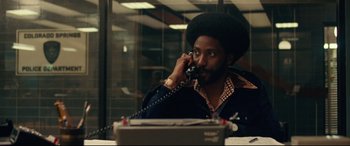 Movie still from “BlacKkKlansman” (2018), directed by Spike Lee – A man talking on a phone while sitting at a desk; Medium shot, Over the shoulder angle