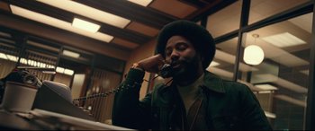 Movie still from “BlacKkKlansman” (2018), directed by Spike Lee – A man talking on a phone while wearing a green jacket; Medium shot, Low angle