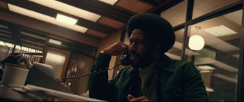 Movie still from “BlacKkKlansman” (2018), directed by Spike Lee – A man talking on a phone while wearing a green jacket; Medium shot, Low angle