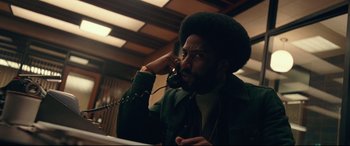 Movie still from “BlacKkKlansman” (2018), directed by Spike Lee – A man talking on a phone while sitting down; Medium shot, Low angle