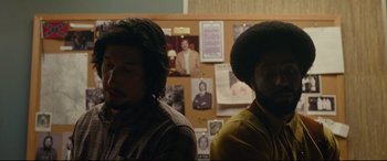Movie still from “BlacKkKlansman” (2018), directed by Spike Lee – Two men standing next to each other in front of a bulletin board; Medium shot, Over the shoulder angle