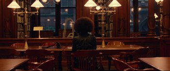 Movie still from “BlacKkKlansman” (2018), directed by Spike Lee – A person sitting at a wooden table in front of a window; Wide shot, Over the shoulder angle