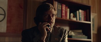 Movie still from “BlacKkKlansman” (2018), directed by Spike Lee – A man talking on a phone while sitting in front of a book shelf; Close Up shot, Low angle