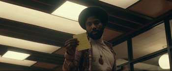 Movie still from “BlacKkKlansman” (2018), directed by Spike Lee – A man holding a piece of paper while standing in a room; Close Up shot, Low angle