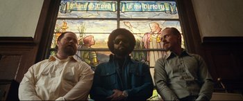 Movie still from “BlacKkKlansman” (2018), directed by Spike Lee – A group of men standing next to each other in front of a stained glass window; Medium shot, Low angle