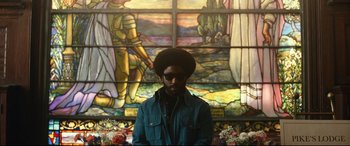 Movie still from “BlacKkKlansman” (2018), directed by Spike Lee – A man standing in front of a stained - glass window; Medium shot, Low angle