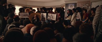 Movie still from “BlacKkKlansman” (2018), directed by Spike Lee – A group of people gathered in a living room; Wide shot, Over the shoulder angle