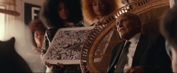 Movie still from “BlacKkKlansman” (2018), directed by Spike Lee – A man sitting in a chair next to two women; Medium shot, Over the shoulder angle