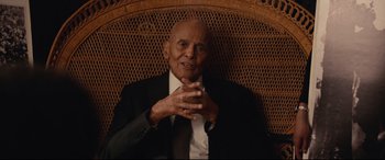 Movie still from “BlacKkKlansman” (2018), directed by Spike Lee – An older man wearing a suit sitting in a wicker chair; Medium shot, Low angle