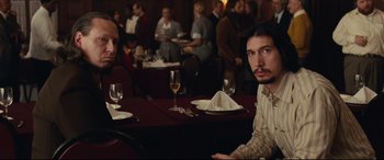 Movie still from “BlacKkKlansman” (2018), directed by Spike Lee – A man sitting at a table in front of a glass of white wine; Medium shot, Over the shoulder angle