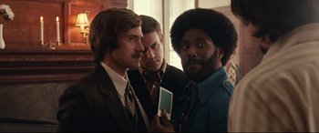 Movie still from “BlacKkKlansman” (2018), directed by Spike Lee – A group of men standing next to each other in a room; Medium shot, Over the shoulder angle