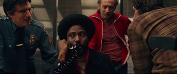 Movie still from “BlacKkKlansman” (2018), directed by Spike Lee – A man in a red jacket talking on a phone; Medium shot, Over the shoulder angle