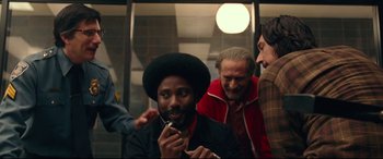 Movie still from “BlacKkKlansman” (2018), directed by Spike Lee – A group of people standing around a man with a beard; Medium shot, Over the shoulder angle