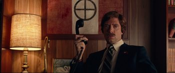 Movie still from “BlacKkKlansman” (2018), directed by Spike Lee – A man in a suit and tie holding up a phone; Medium shot, Low angle