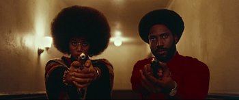 Movie still from “BlacKkKlansman” (2018), directed by Spike Lee – A couple of people that are holding guns in a room; Medium shot, Low angle