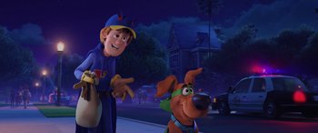 Movie still from “Scoob!” (2020), directed by Tony Cervone – A man and a dog are standing next to each other in front of a building; Medium shot, Over the shoulder angle