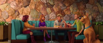 Movie still from “Scoob!” (2020), directed by Tony Cervone – A group of people sitting at a table eating food; Wide shot, Over the shoulder angle