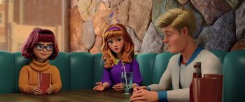 Movie still from “Scoob!” (2020), directed by Tony Cervone – A girl and a boy sitting at a table with a glass; Medium shot, Over the shoulder angle